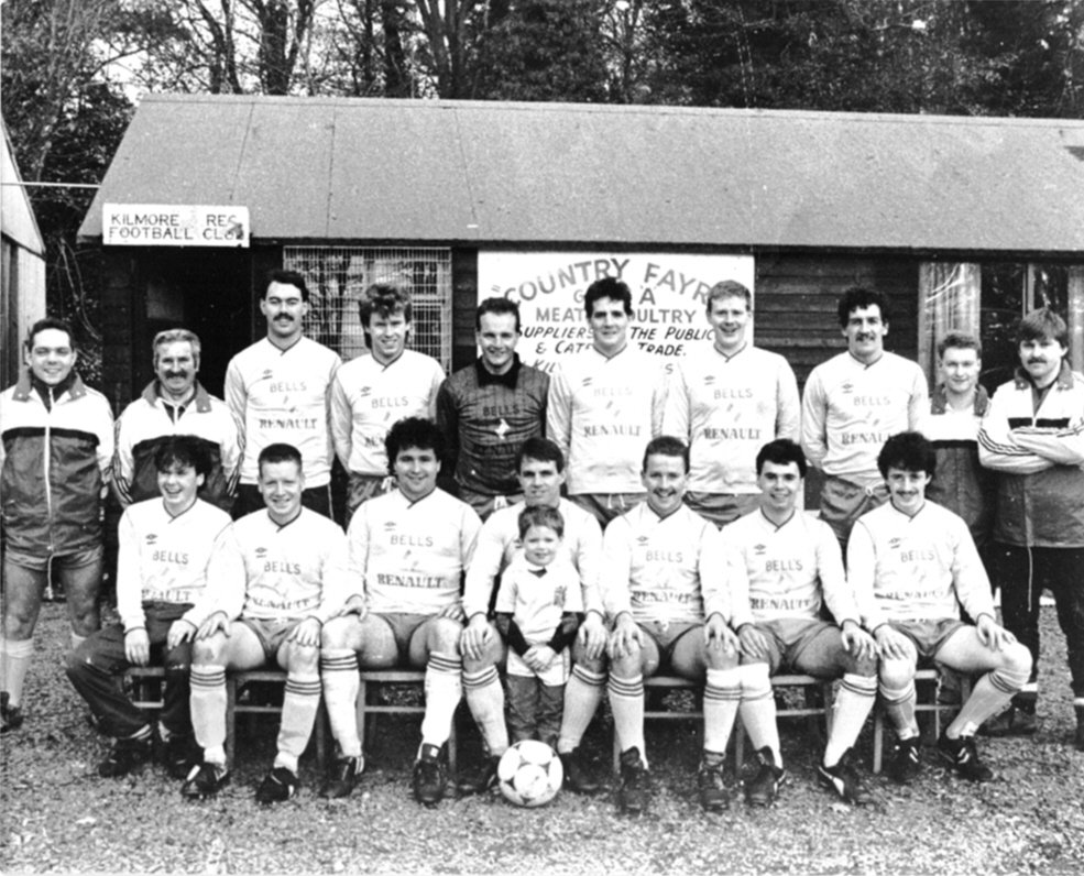 The first team outside the clubhouse at Crossgar in the Bells and Renault strip, catalogued as 1987-88. Back, from left: Davy Graham, Wilbert Morrow, one still to name, Stephen Rodgers, "Burger" Brennan, Conleth McCarthy, Paul Moore, Noel McCarthy, one still to name, Tom Kennedy. Front: two still to name, Sean Bell, Mel McCarthy, Kieran Bell, Johnny Montgomery, one still to name.